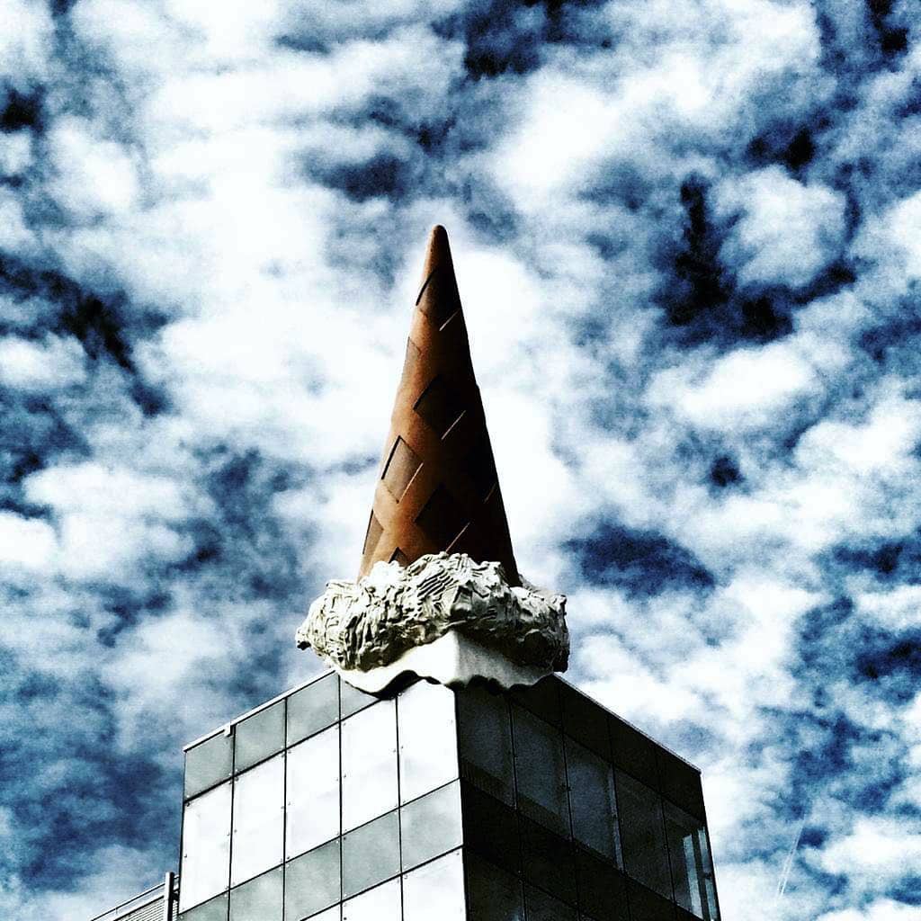 Nou, wat is er nu gebeurd? 🤭🍦 “Dropped cone”, gemaakt door het kunstenaarsstel Coosje van Bruggen en Claes Oldenburg, ligt al sinds maart 2001 op het dak van de Neumarktgallerie in Keulen.  Zoals vele Pop-Art kunstwerken is dit ijsje een ironische kritiek op de consumptiemaatschappij. 🍬☝️ En als je nog een keer kijkt, doet de ijswafel je ook aan een kerktoren denken, waarvan je er in het silhouet van Keulen sowieso heel veel kunt ontdekken. 
Opvallend is het in ieder geval, daar ga je niet zomaar aan voorbij.  #keulen #publiekekunst #ijsje #popart #claesoldenburg #coosjevanbruggen #droppedcone #grappig #vakantieinduitsland #dagjeduitsland #dagjeuit #uitstapje #cultuur #duitslandmagazine