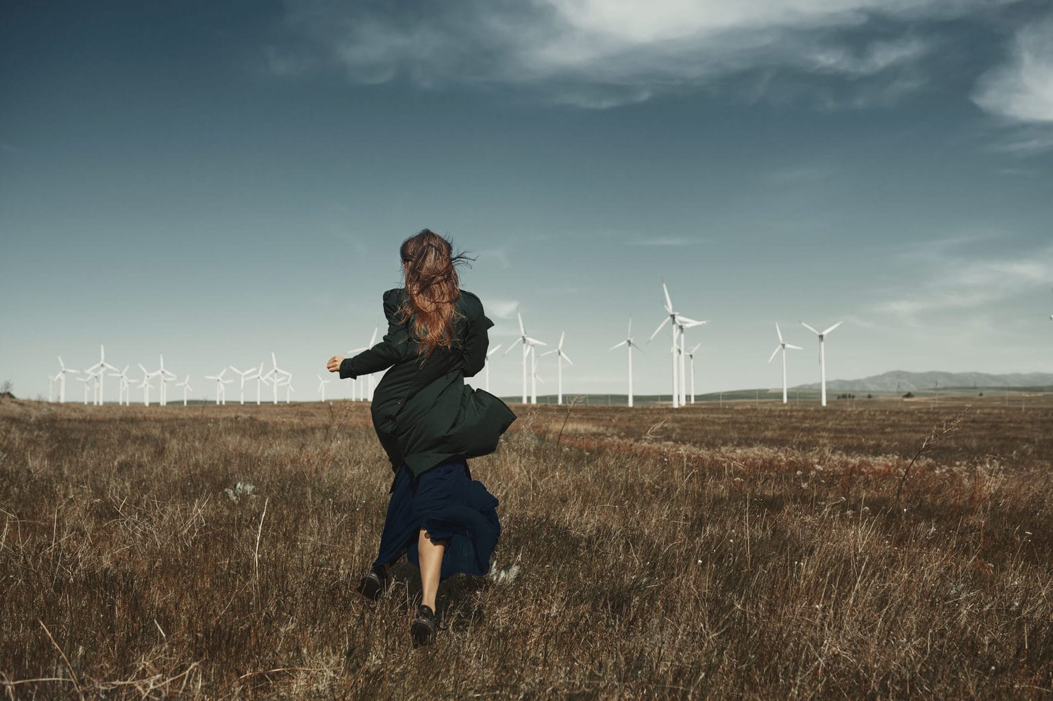 Vrouw loopt door een veld in richting van eindturbine als symbool voor duurzame mode uit Duitsland