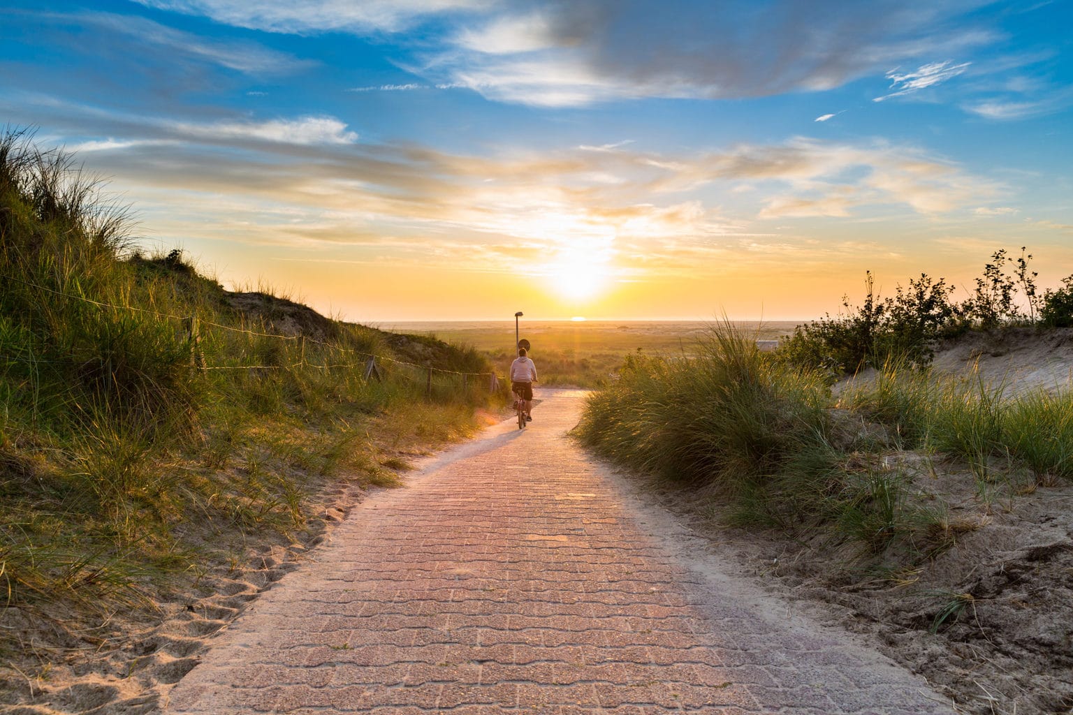 Fietser in de duinen op het eiland Borkum in Duitsland tijdens zonondergang