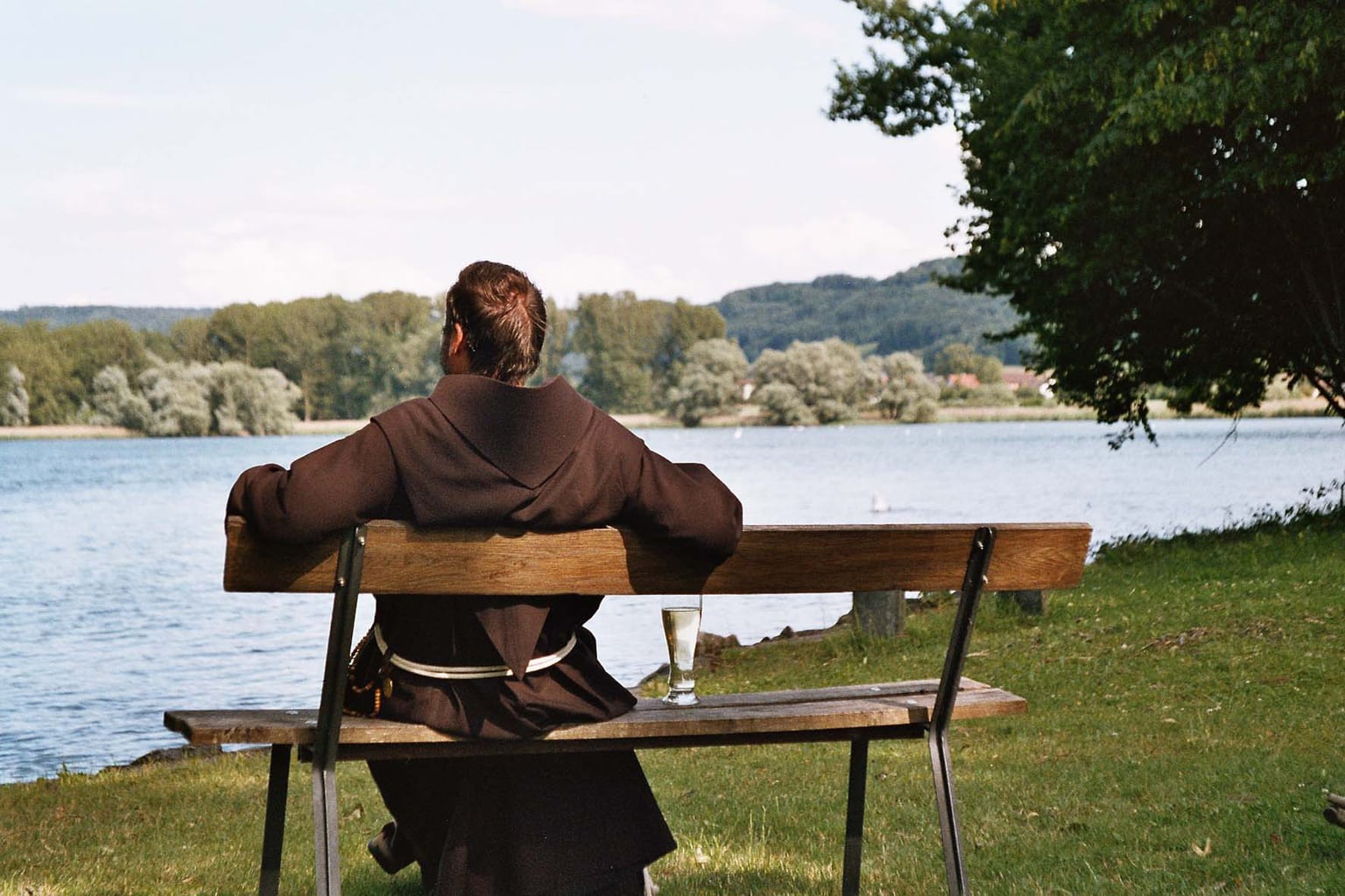 Een monnik met een glas water kijkt dromerig op de Bodensee