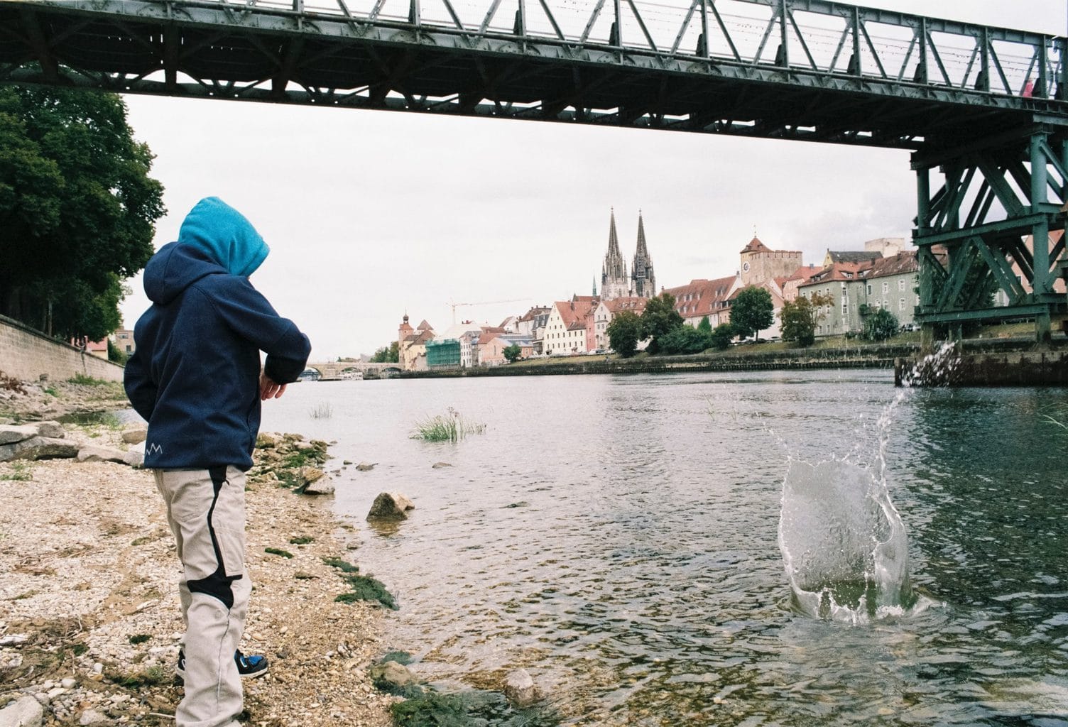 Jonge gooit steentjes aan de Donau in Regensburg