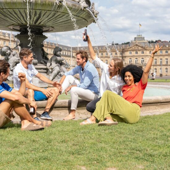 5 mensen zitten voor een fontein op de Schlossplatz in Stuttgart, Duitsland en praten.