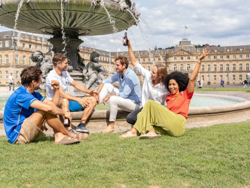 5 mensen zitten voor een fontein op de Schlossplatz in Stuttgart, Duitsland en praten.