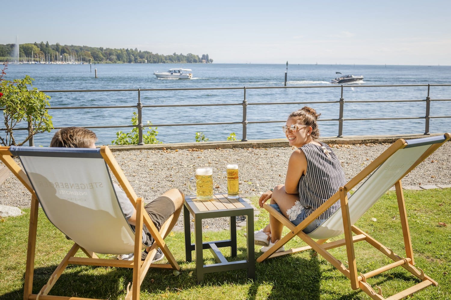 Twee bierdrinkende mensen voor een eilandhotel met uitzicht op ligstoelen aan het Bodenmeer in Konstanz, Duitsland