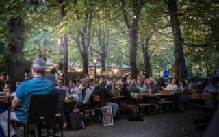 Het is erg druk in de Hofbräukeller in München. Mensen zitten op bankjes in de biertuin onder de groene bomen in de Duitse stad.