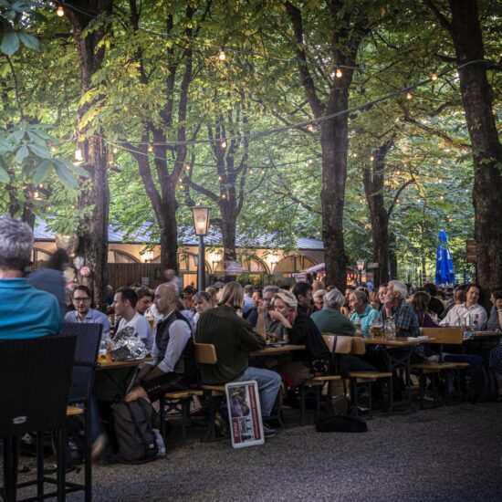 Het is erg druk in de Hofbräukeller in München. Mensen zitten op bankjes in de biertuin onder de groene bomen in de Duitse stad.