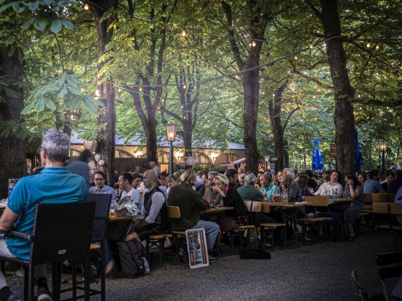 Het is erg druk in de Hofbräukeller in München. Mensen zitten op bankjes in de biertuin onder de groene bomen in de Duitse stad.