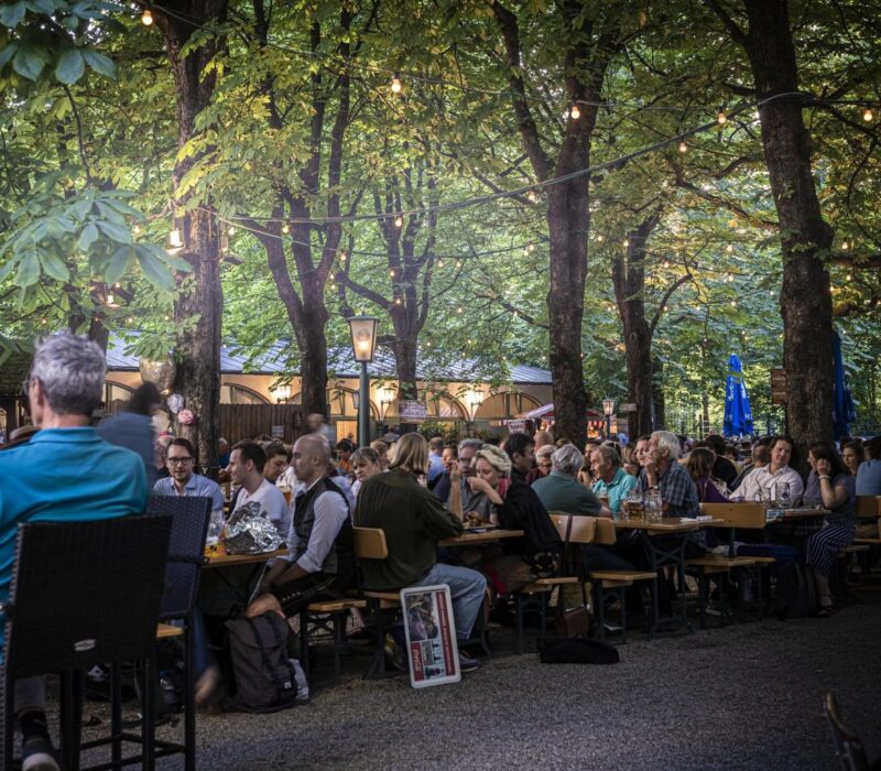 Het is erg druk in de Hofbräukeller in München. Mensen zitten op bankjes in de biertuin onder de groene bomen in de Duitse stad.