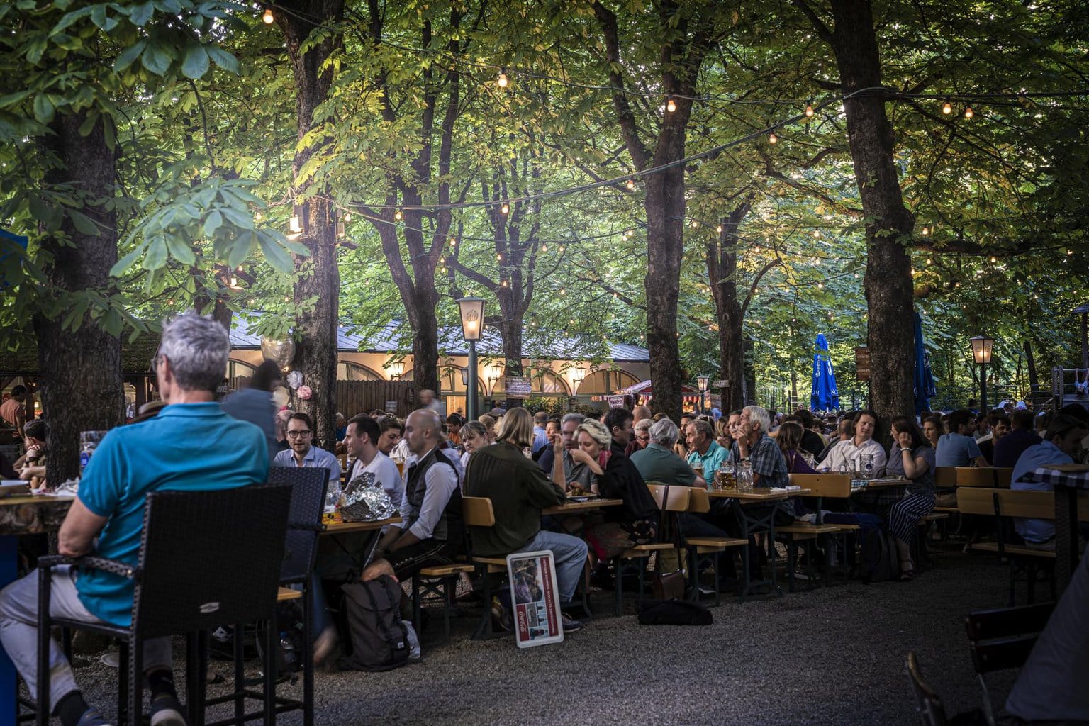 Het is erg druk in de Hofbräukeller in München. Mensen zitten op bankjes in de biertuin onder de groene bomen in de Duitse stad.