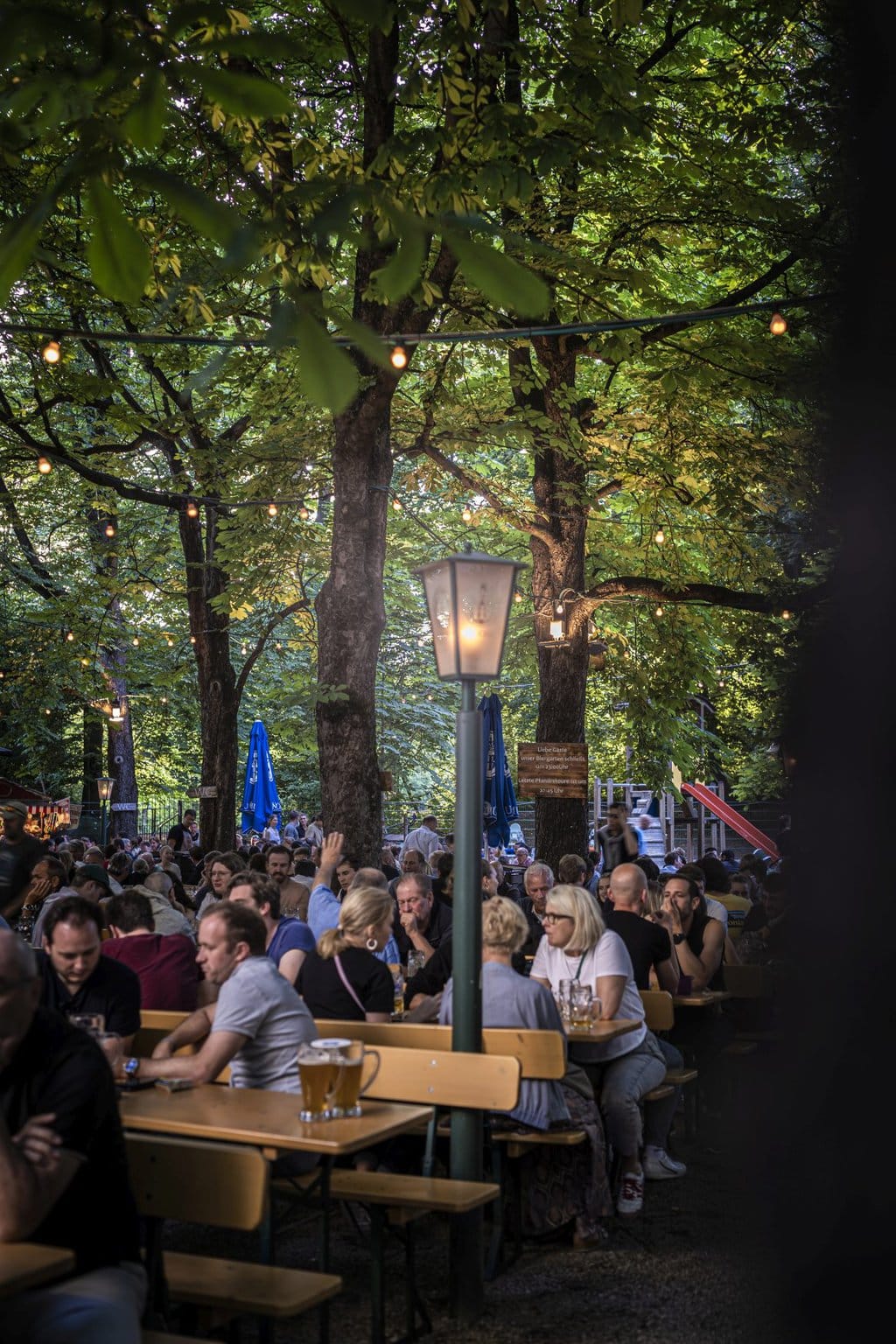 Het is erg druk in de Hofbräukeller in München. Mensen zitten op bankjes in de biertuin onder de groene bomen in de Duitse stad.