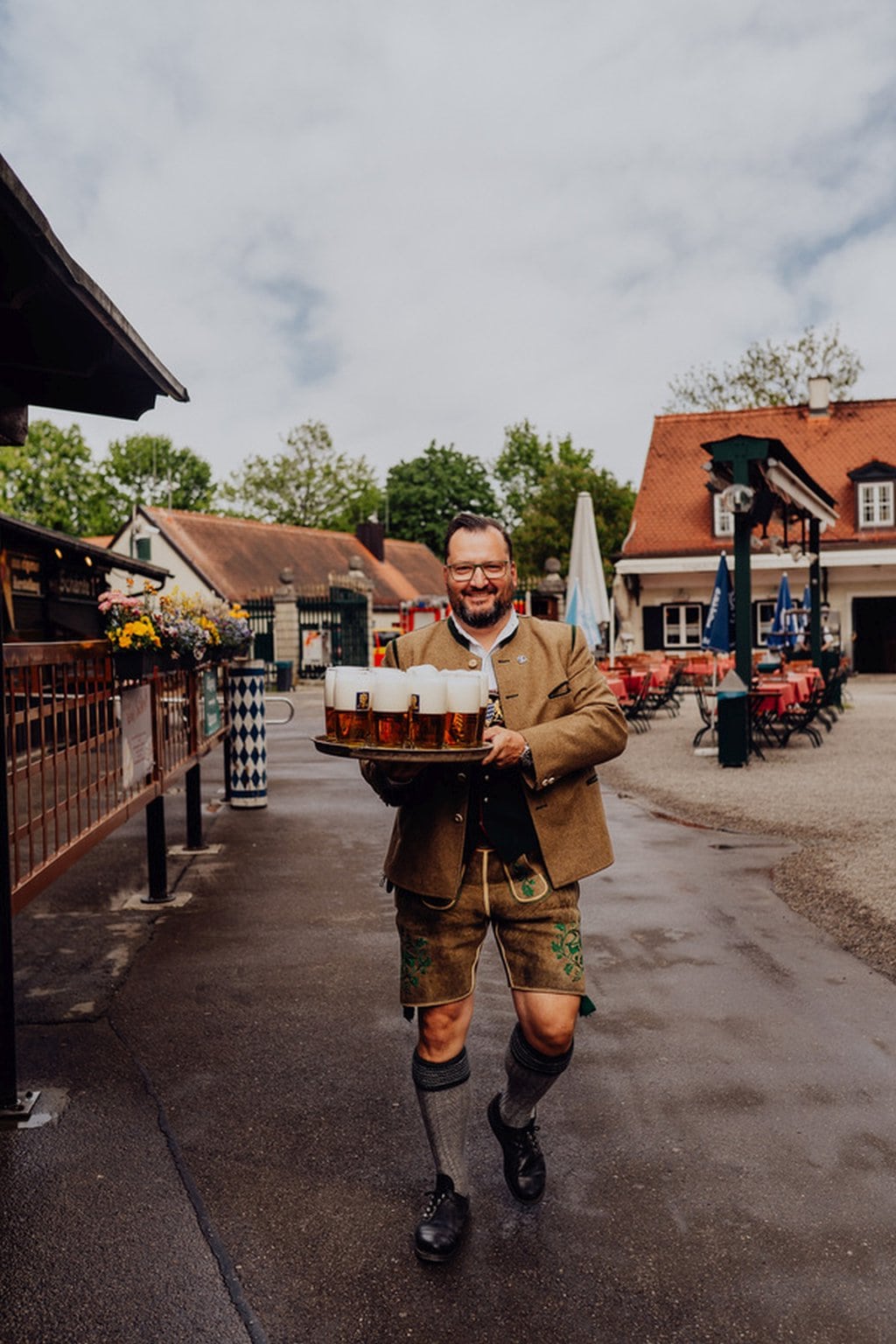 Een man staat op straat in München met een lederhose aan en glazen bier op een tablet