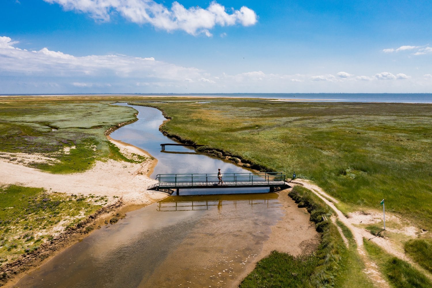 Persoon loopt op een brug tussen kwelders op Borkum, een Duits eiland