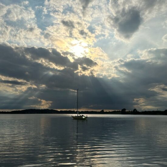 Zon schijnt door de wolken boven een zeilboot op de Schlei in Sleeswijk-Holstein, Duitsland