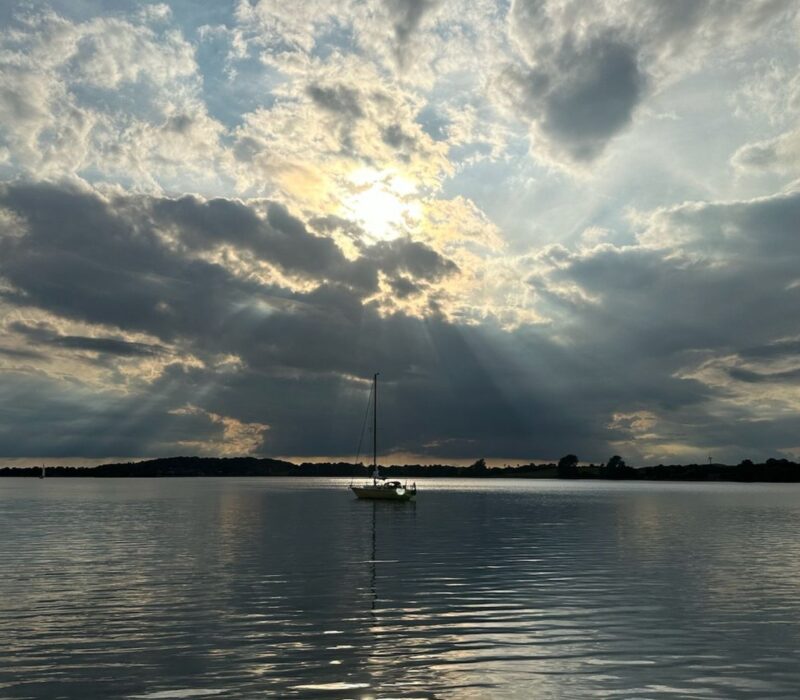 Zon schijnt door de wolken boven een zeilboot op de Schlei in Sleeswijk-Holstein, Duitsland