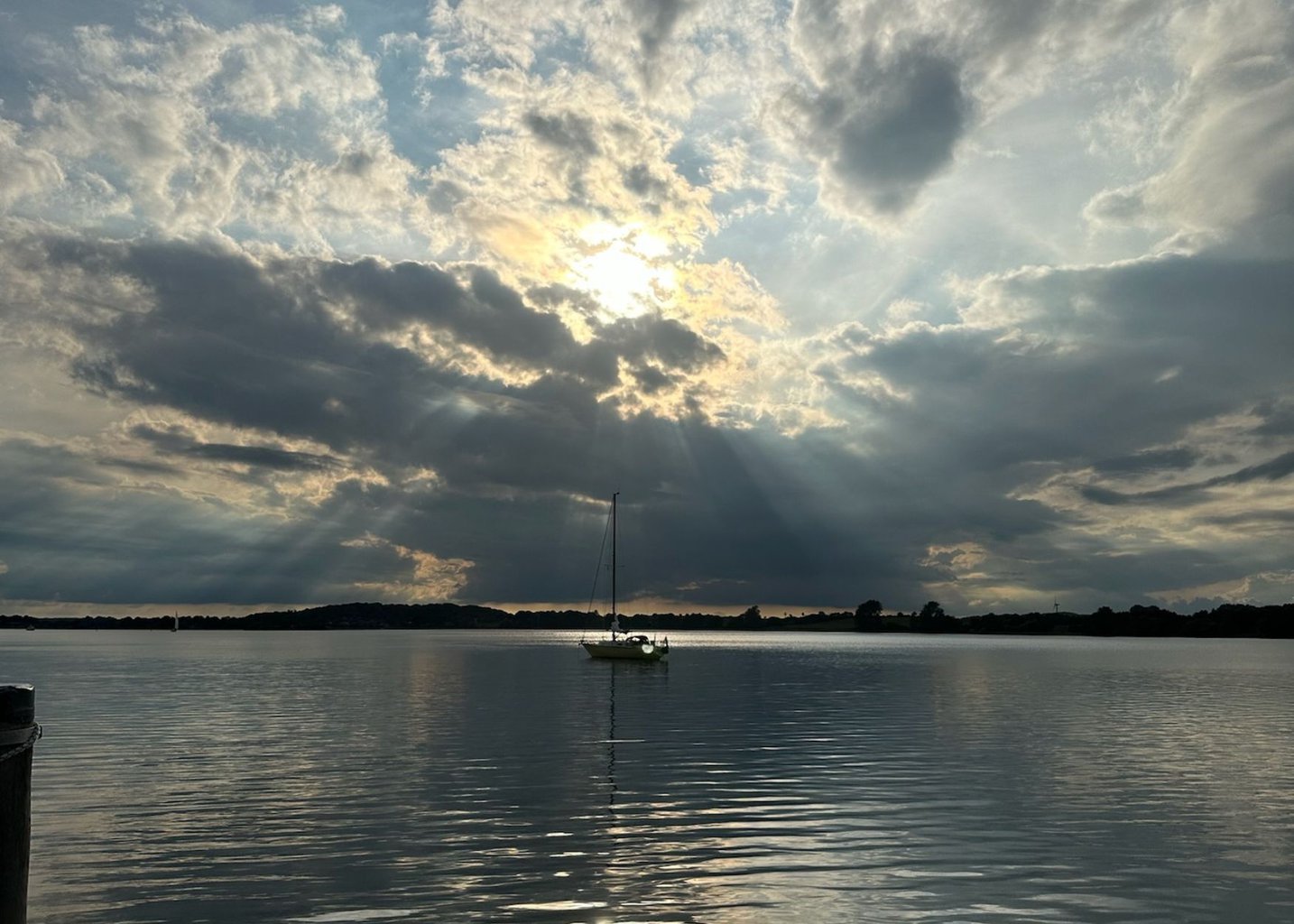 Zon schijnt door de wolken boven een zeilboot op de Schlei in Sleeswijk-Holstein, Duitsland