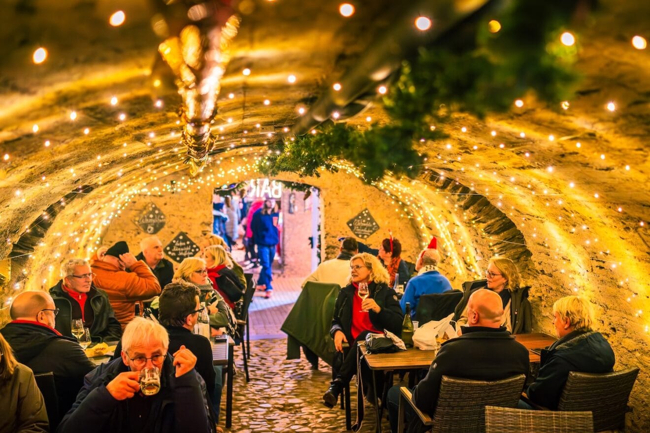 Bezoekers met glühwein in de verlichte wijnkelders van de Mosel-Wein-Nachts-Markt in Traben-Trarbach