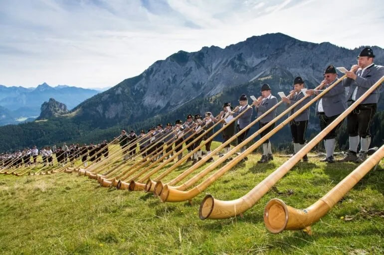 Mannen in lederhosen in de Allgäu spelen alpenhoorns in de Alpen in Beieren, Duitsland