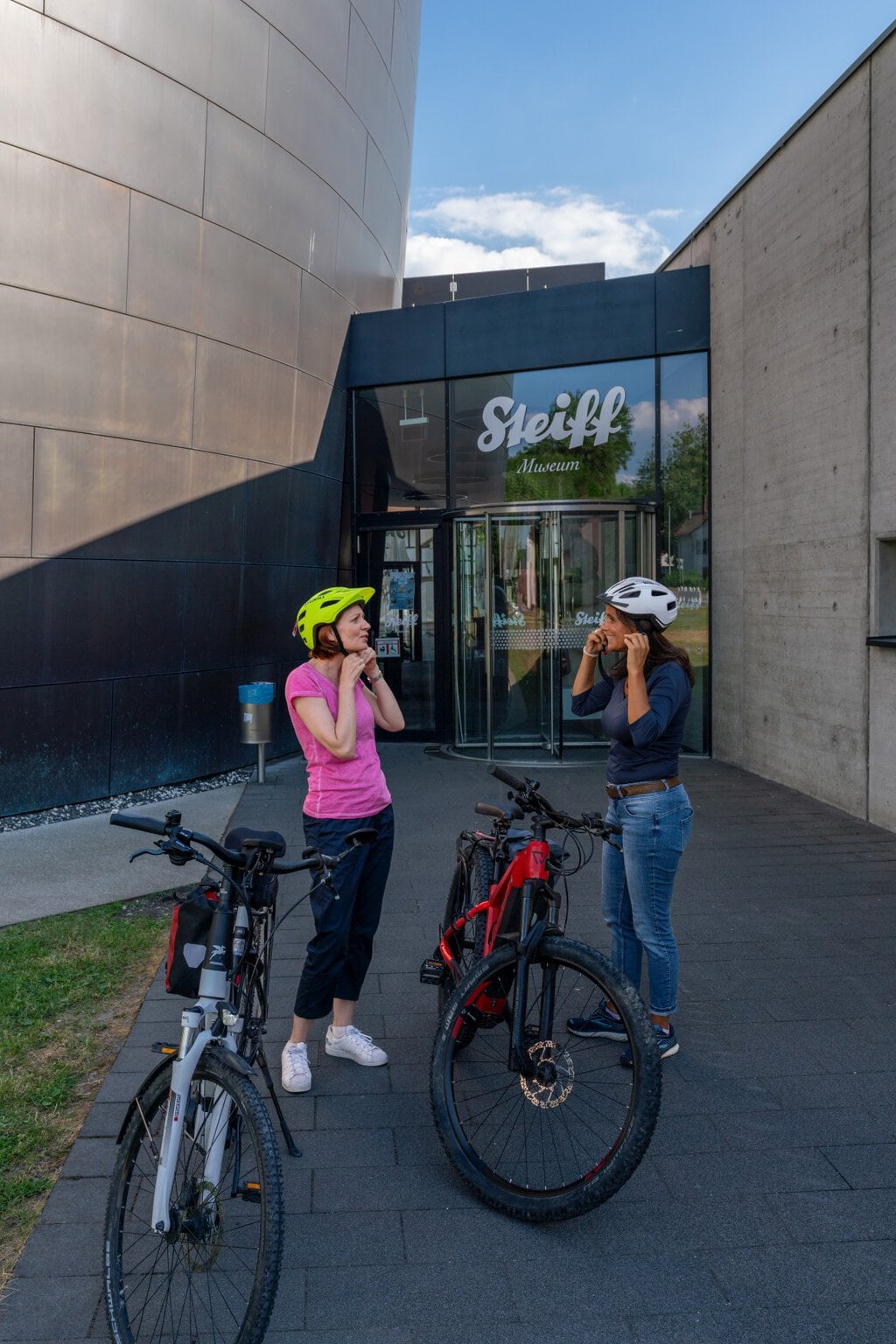 Simone Gulkowski en Julia Neidhardt staan met hun fietsen voor het Steiff Museum in Giengen an der Brenz, Baden-Württemberg, Duitsland