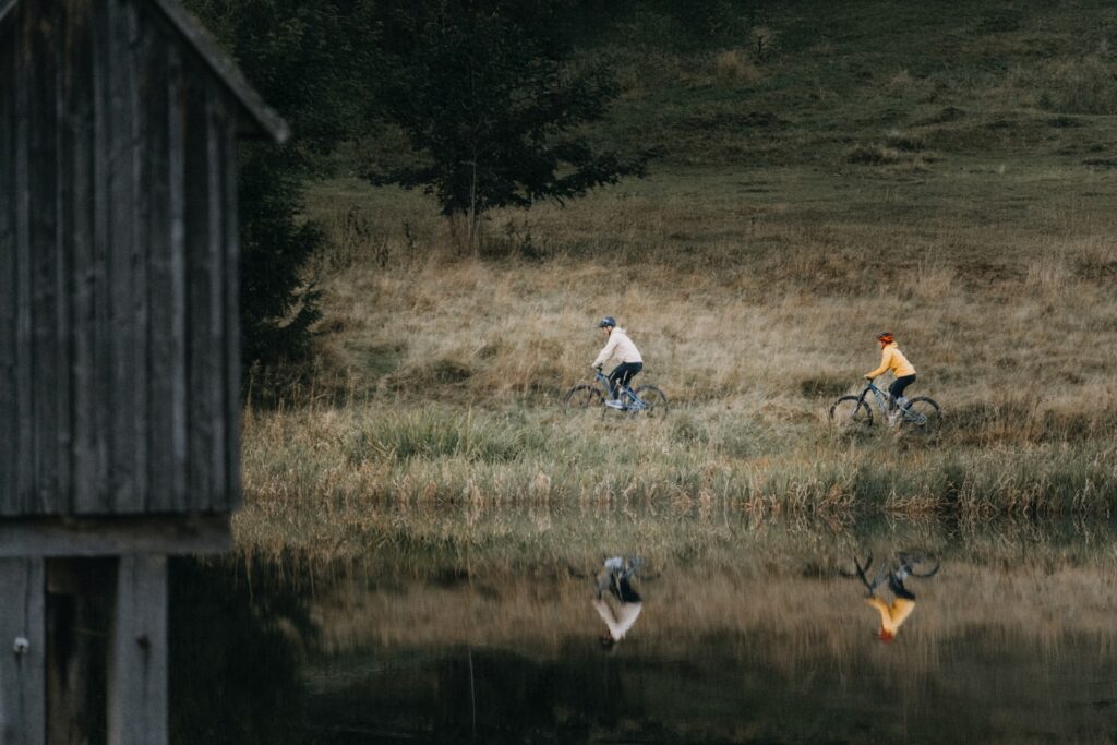Wildwood Camping in de Harz: twee fietsers rijden langs een spiegelglad bergmeer, omringd door ruige natuur – een idyllisch moment van Vanlife midden in Duitsland.