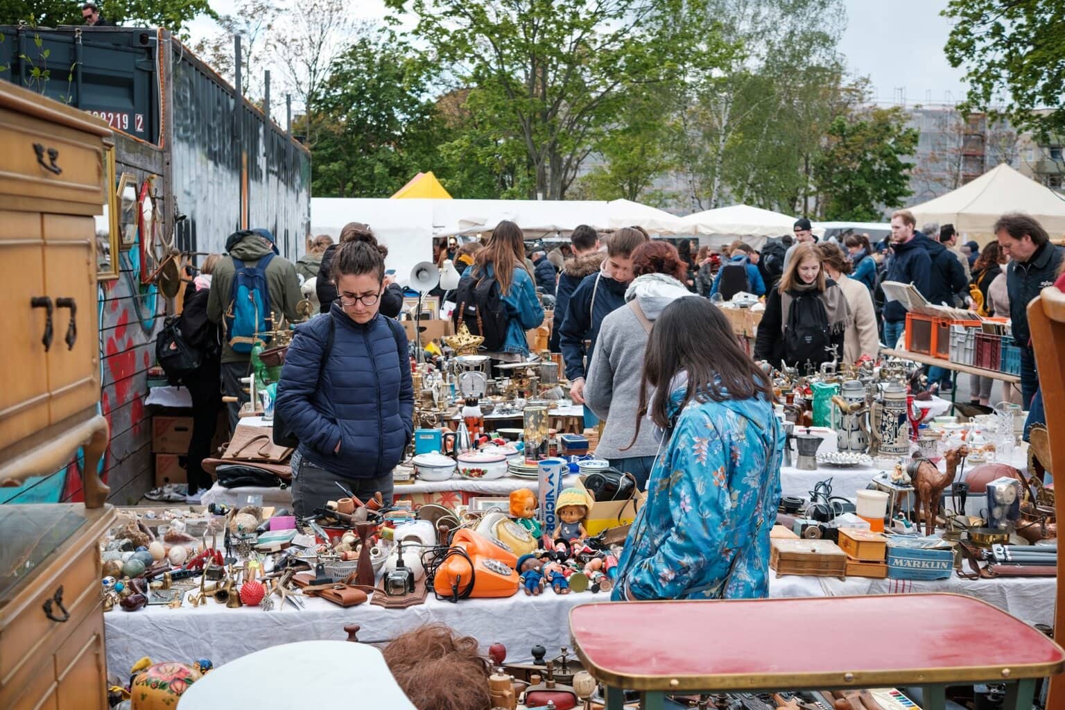 Drukke vlooienmarkt in Berlijn met bezoekers die rondsnuffelen tussen retro huishoudelijke spullen, antiek en tweedehands curiosa onder witte kraampjes – typisch voor populaire vlooienmarkten in Duitsland.
