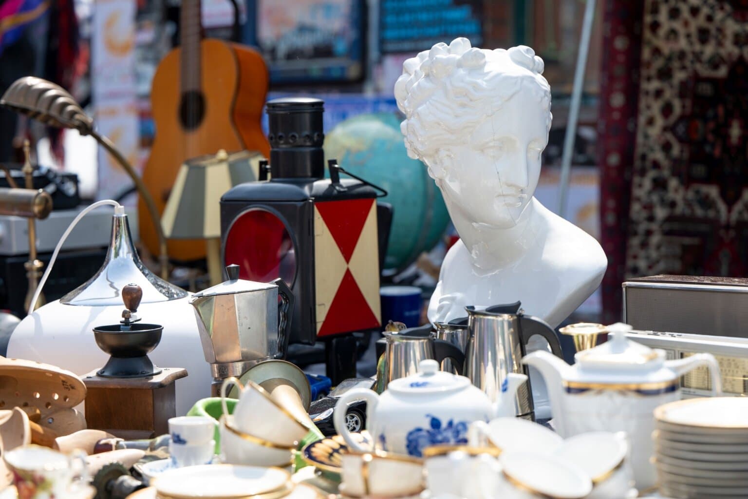 Kraam op een vlooienmarkt in Hamburg aan de Flohschanze met porseleinen beeld, vintage servies, koffiepotten, lampen en een oude lantaarn – een stijlvol voorbeeld van de verrassende vondsten op vlooienmarkten in Duitsland.