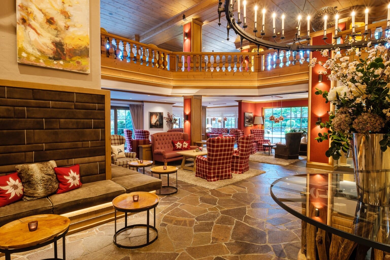 Warme en sfeervolle lobby van het Sonnenalp Resort in Ofterschwang, met houten accenten, Alpenstijl-meubilair en gezellige zitjes in rood geruite stof. Deze uitnodigende ontvangsthal weerspiegelt de authentieke charme en hoogwaardige service van het beste luxehotel van Duitsland, perfect voor ontspanning in een elegante bergomgeving.