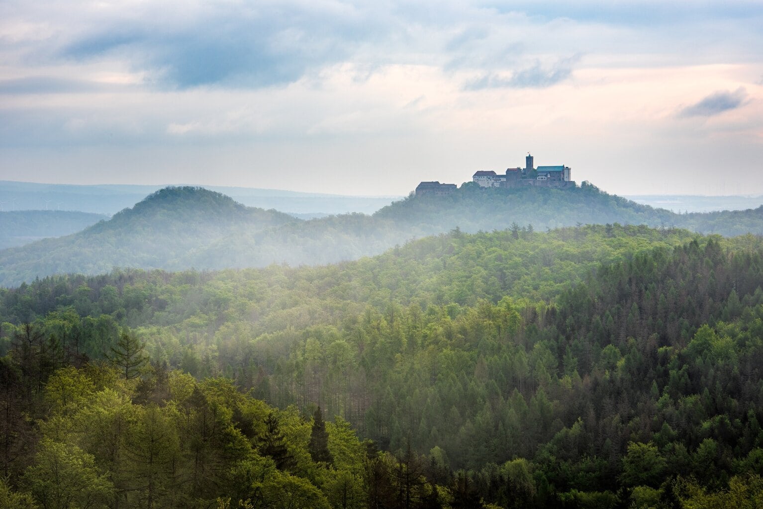 Uitzicht op de met nevel bedekte bossen van het Thüringer Woud met de Wartburg op de heuveltop – een inspirerende locatie voor Waldbäder in Duitsland en natuurlijke rust.