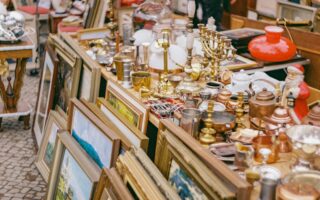 Oude schilderijlijsten, kandelaars, koperwerk, lampen en kerstdecoratie op een rommelige kraam – een typisch tafereel op sfeervolle vlooienmarkten in Duitsland, waar vintage en curiosa elkaar ontmoeten.