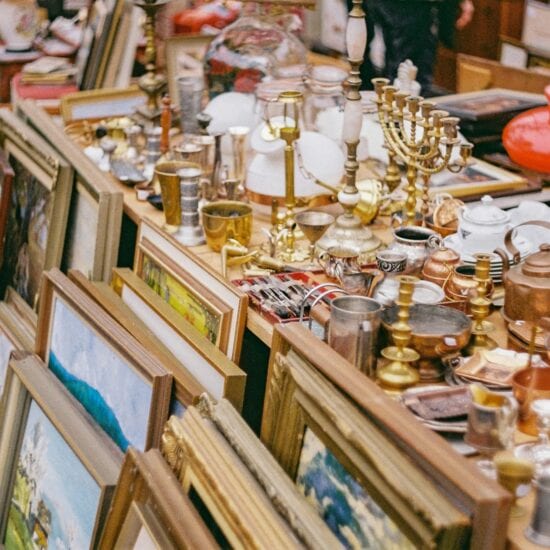 Oude schilderijlijsten, kandelaars, koperwerk, lampen en kerstdecoratie op een rommelige kraam – een typisch tafereel op sfeervolle vlooienmarkten in Duitsland, waar vintage en curiosa elkaar ontmoeten.