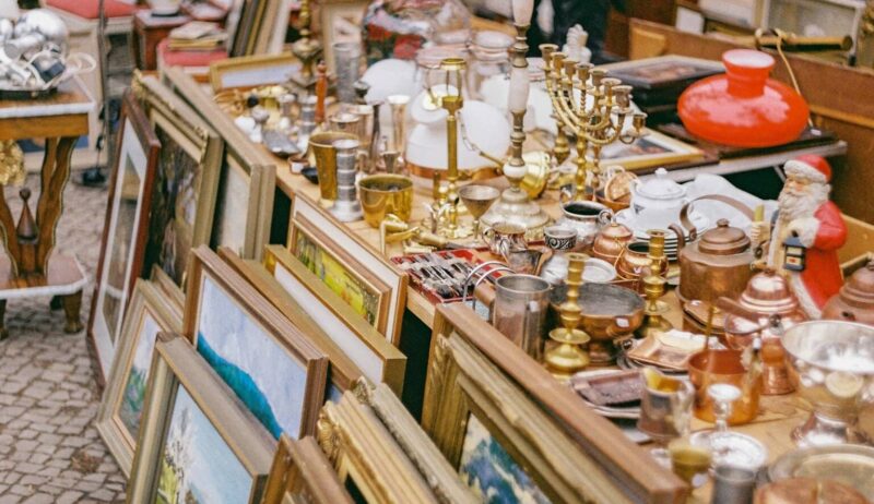 Oude schilderijlijsten, kandelaars, koperwerk, lampen en kerstdecoratie op een rommelige kraam – een typisch tafereel op sfeervolle vlooienmarkten in Duitsland, waar vintage en curiosa elkaar ontmoeten.