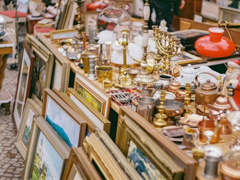 Oude schilderijlijsten, kandelaars, koperwerk, lampen en kerstdecoratie op een rommelige kraam – een typisch tafereel op sfeervolle vlooienmarkten in Duitsland, waar vintage en curiosa elkaar ontmoeten.