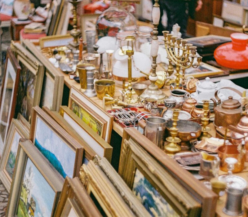 Oude schilderijlijsten, kandelaars, koperwerk, lampen en kerstdecoratie op een rommelige kraam – een typisch tafereel op sfeervolle vlooienmarkten in Duitsland, waar vintage en curiosa elkaar ontmoeten.
