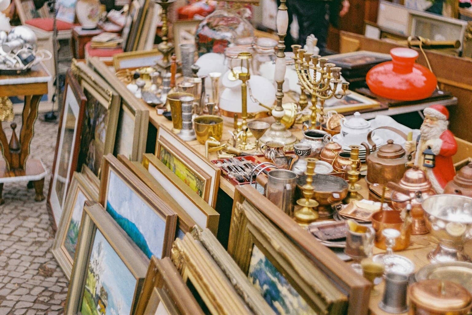 Oude schilderijlijsten, kandelaars, koperwerk, lampen en kerstdecoratie op een rommelige kraam – een typisch tafereel op sfeervolle vlooienmarkten in Duitsland, waar vintage en curiosa elkaar ontmoeten.