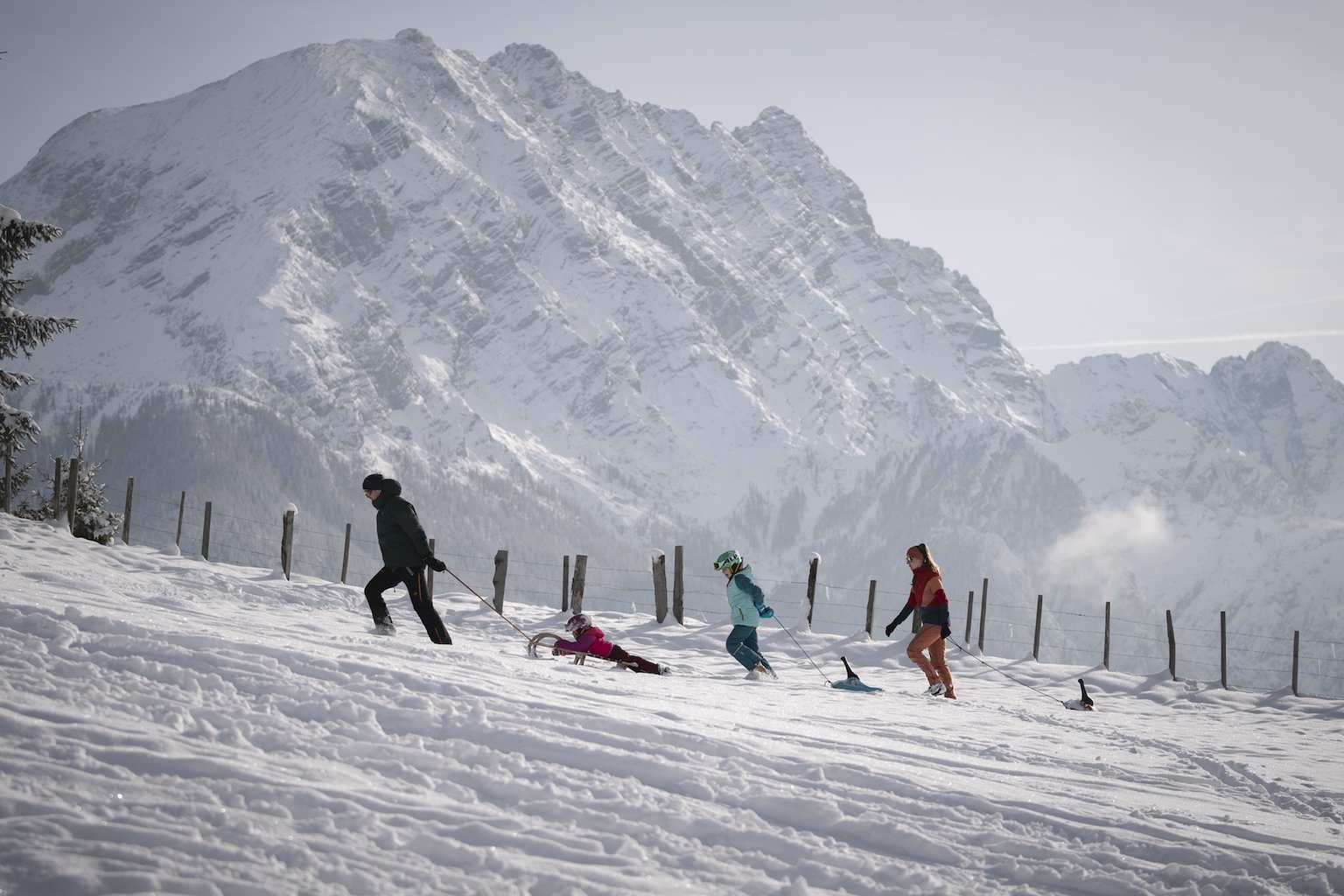 Gezin trekt met sleeën door het besneeuwde winterlandschap van Berchtesgaden, met op de achtergrond imposante Alpentoppen – een sportieve winterdag in het zuiden van Duitsland.