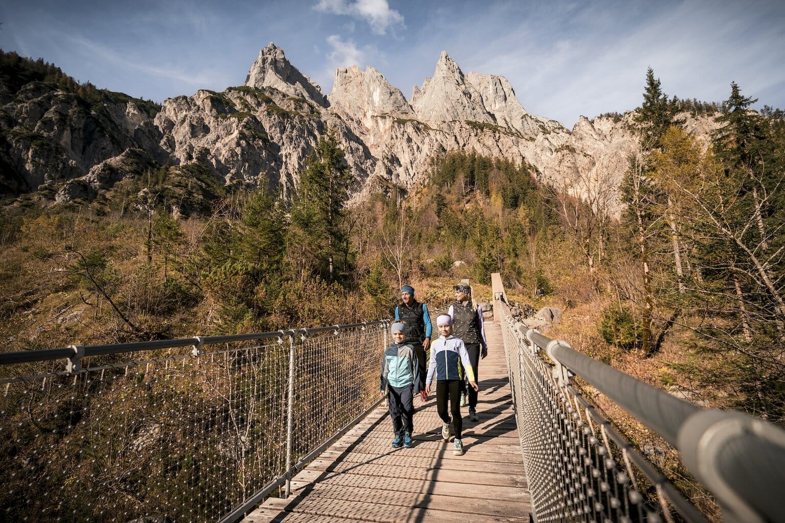 Gezin tijdens een herfstwandeling over een houten brug in Berchtesgaden, met grillige Alpentoppen en kleurrijk berglandschap – ideaal voor wie houdt van wandelen, natuur en vakantie in Duitsland in het hart van Beieren.