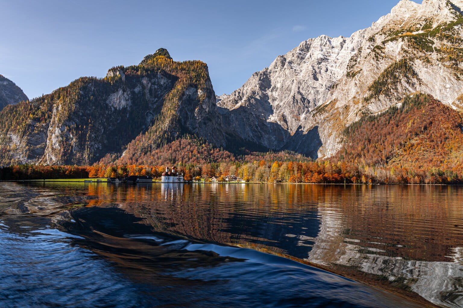Herfstkleuren weerspiegelen in het heldere water van de Königssee in Berchtesgaden, met de barokke kapel van St. Bartholomä en imposante Alpentoppen op de achtergrond – een magisch seizoen in het schilderachtige berchtesgaden.
