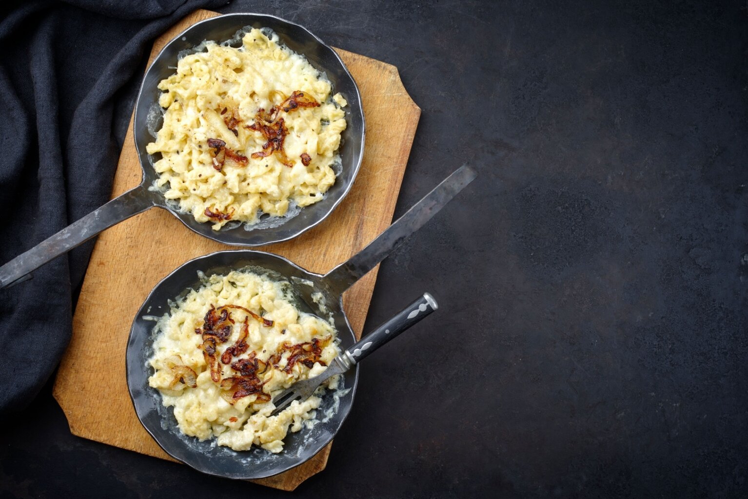 Twee pannen met vers bereide Käsespätzle – een smeuïg, traditioneel gerecht uit Zuid-Duitsland met gesmolten kaas en goudbruin gebakken uien.