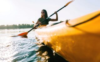 Vrouw peddelt in een gele kano over een zonovergoten rivier tijdens een zomerse tocht – een typisch moment voor actieve kanotochten Duitsland.