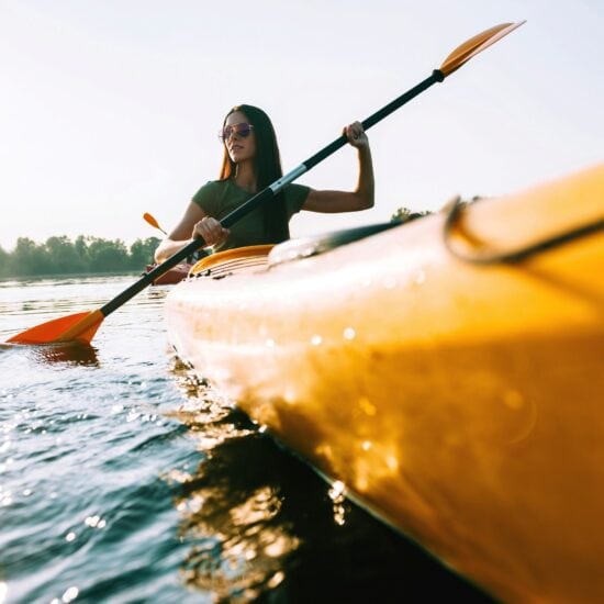 Vrouw peddelt in een gele kano over een zonovergoten rivier tijdens een zomerse tocht – een typisch moment voor actieve kanotochten Duitsland.