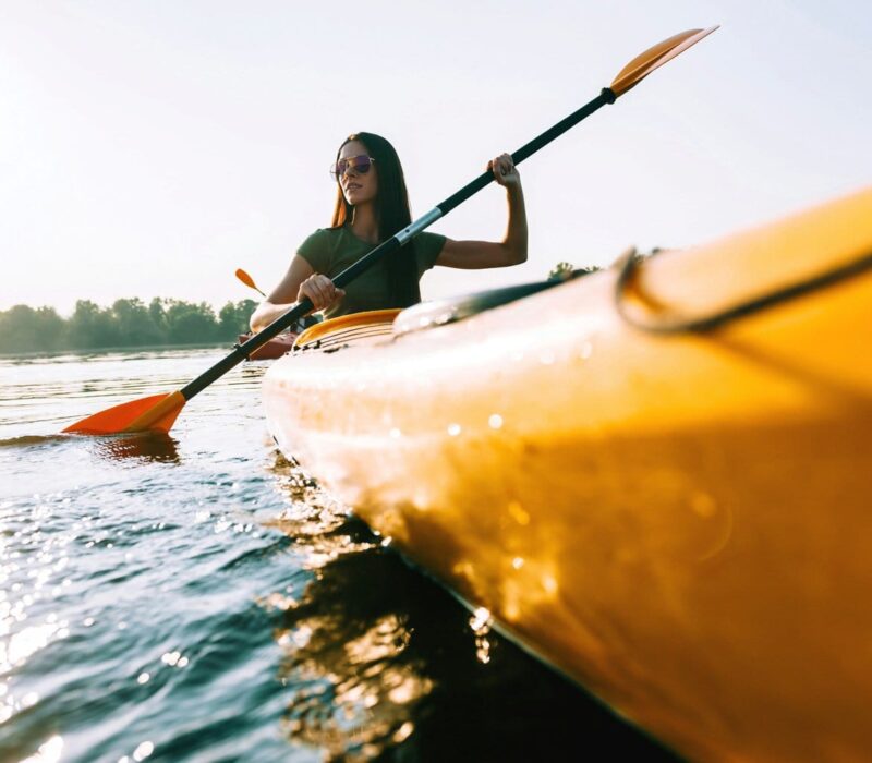 Vrouw peddelt in een gele kano over een zonovergoten rivier tijdens een zomerse tocht – een typisch moment voor actieve kanotochten Duitsland.