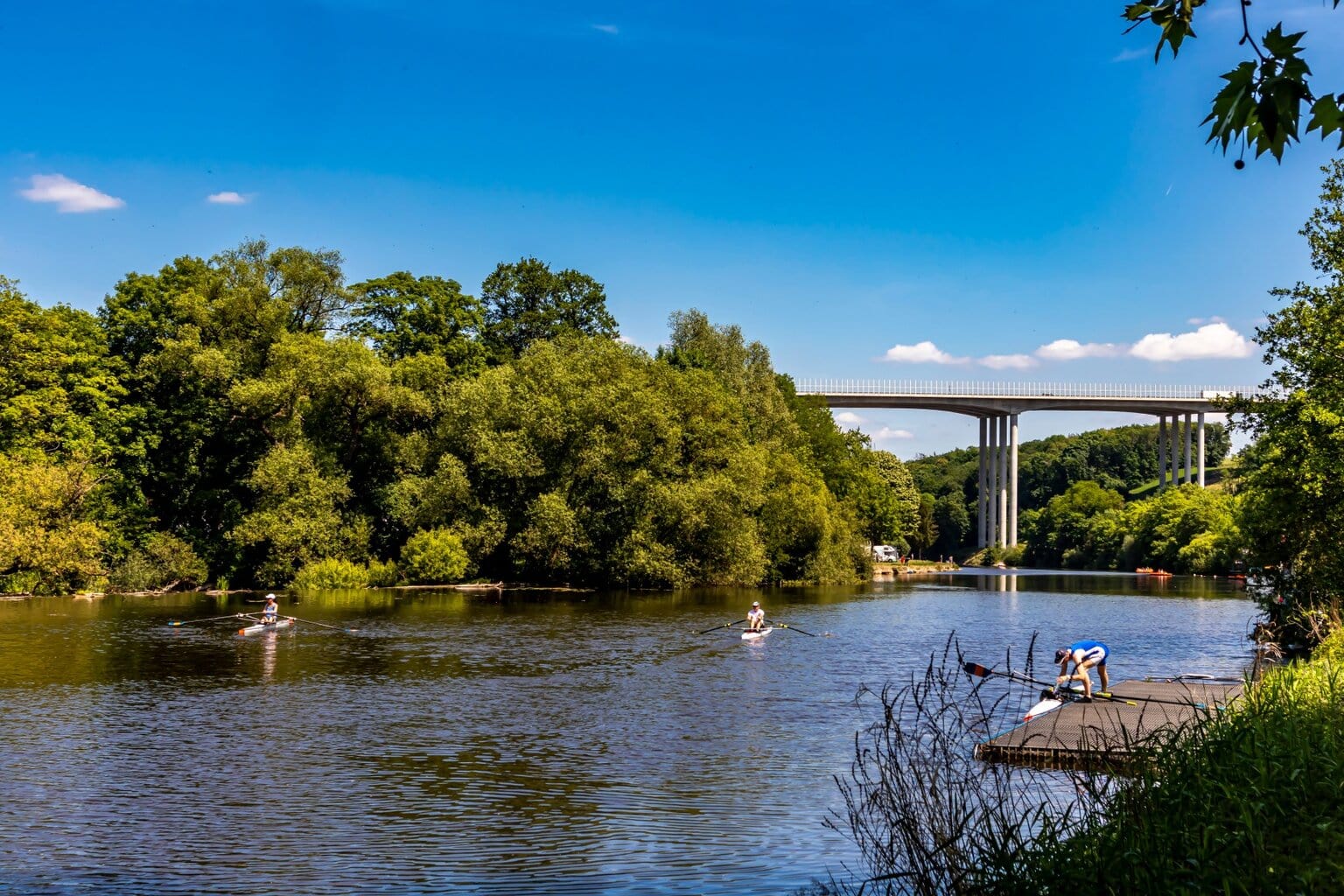 Kanoërs op een rustige rivier onder een hoge brug in een groen landschap – een typisch tafereel van de ontspannen kanotochten Duitsland in de zomer.