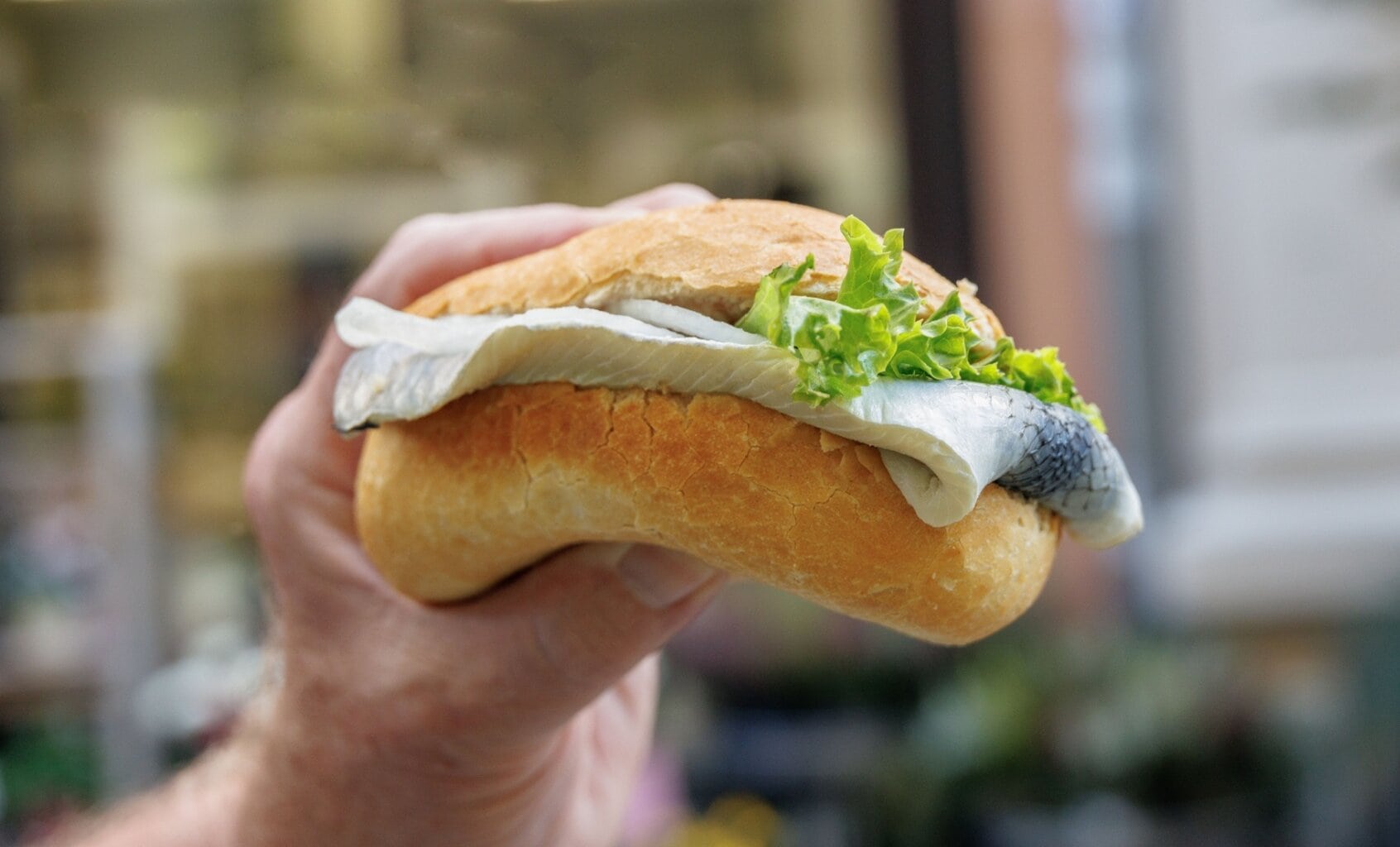 Een hand houdt een vers bereid visbroodje met haring en sla omhoog – een eenvoudige maar geliefde streetfoodklassieker onder de typisch Duitse gerechten, vooral aan de Noordzeekust.