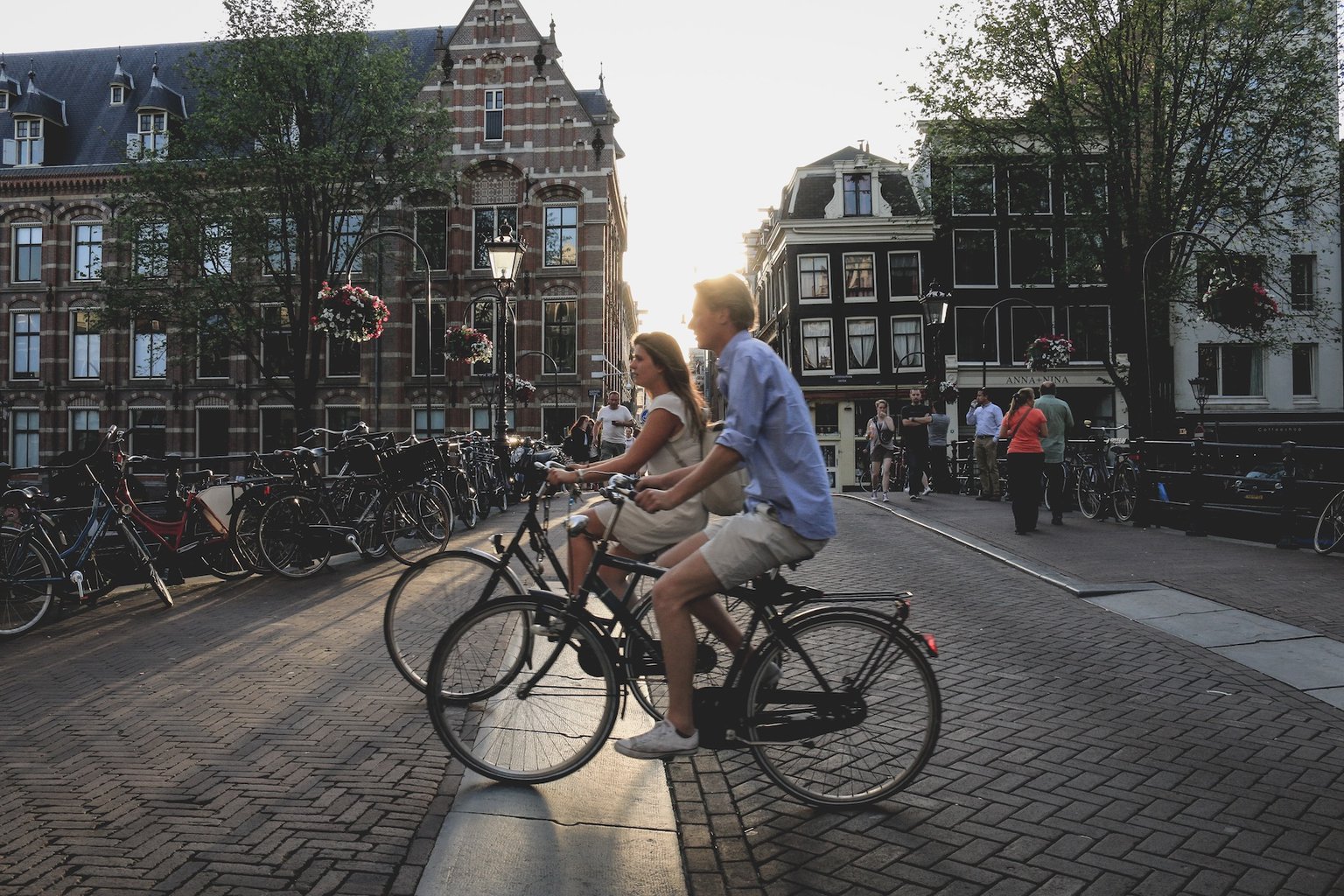 Fietsers in het avondlicht op een Amsterdamse gracht – het startpunt van de Oranjeroute, die van Nederland naar Duitsland leidt langs koninklijke sporen en historische steden.