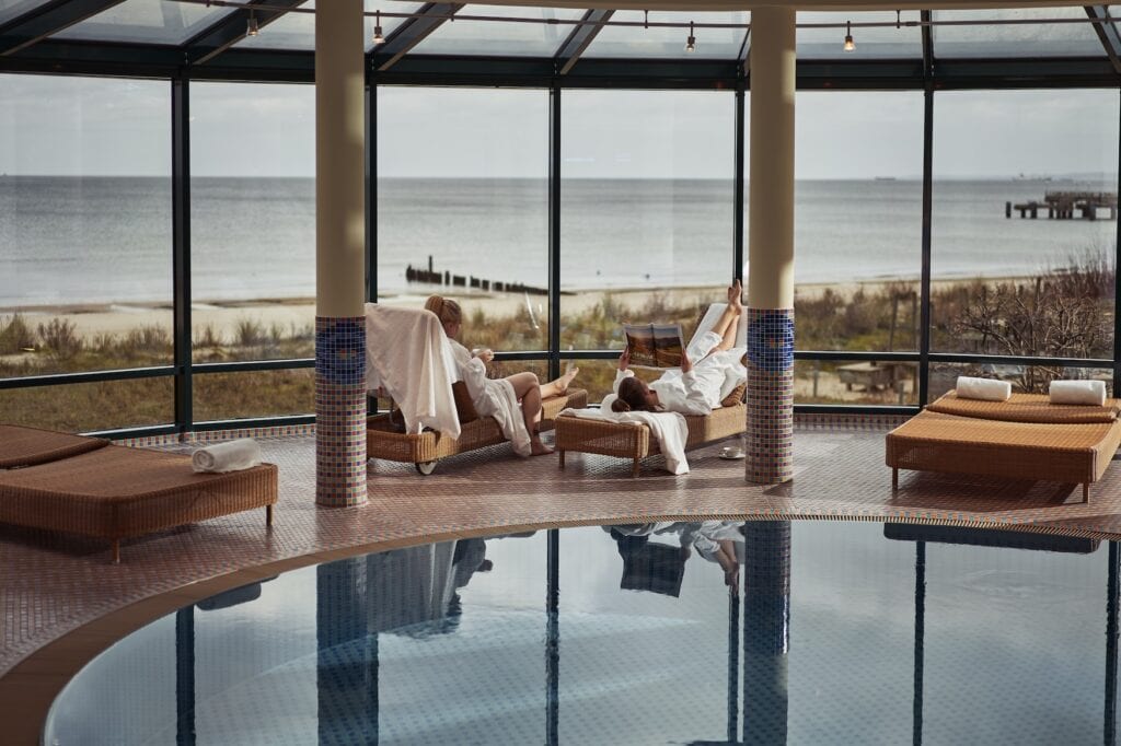 Het Spa van het aja Strandhotel Bansin. Twee Personen liggen op ligstoelen en lezen een tijdschrift met uitzicht op de Oostzee
