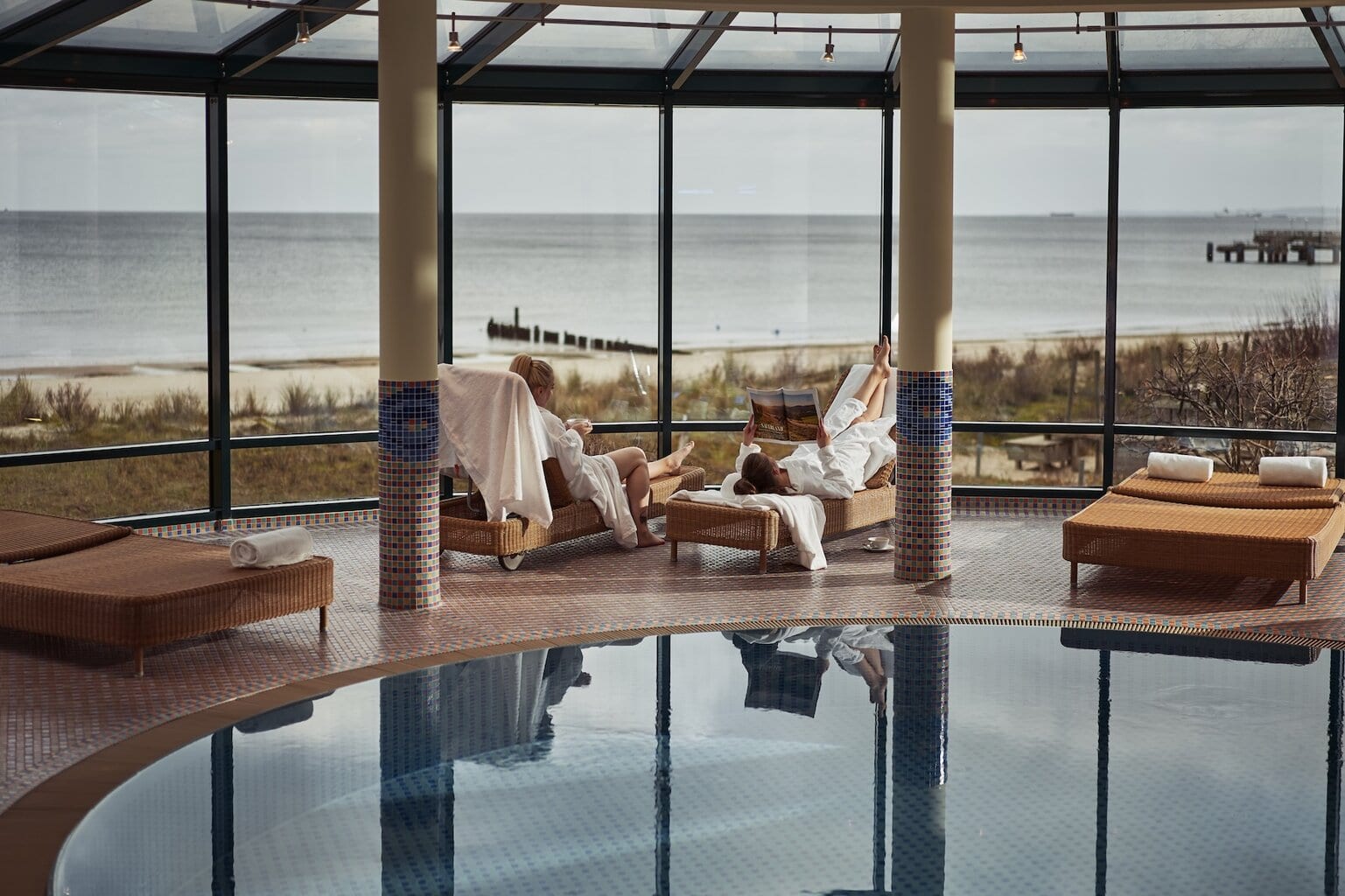 Het Spa van het aja Strandhotel Bansin. Twee Personen liggen op ligstoelen en lezen een tijdschrift met uitzicht op de Oostzee