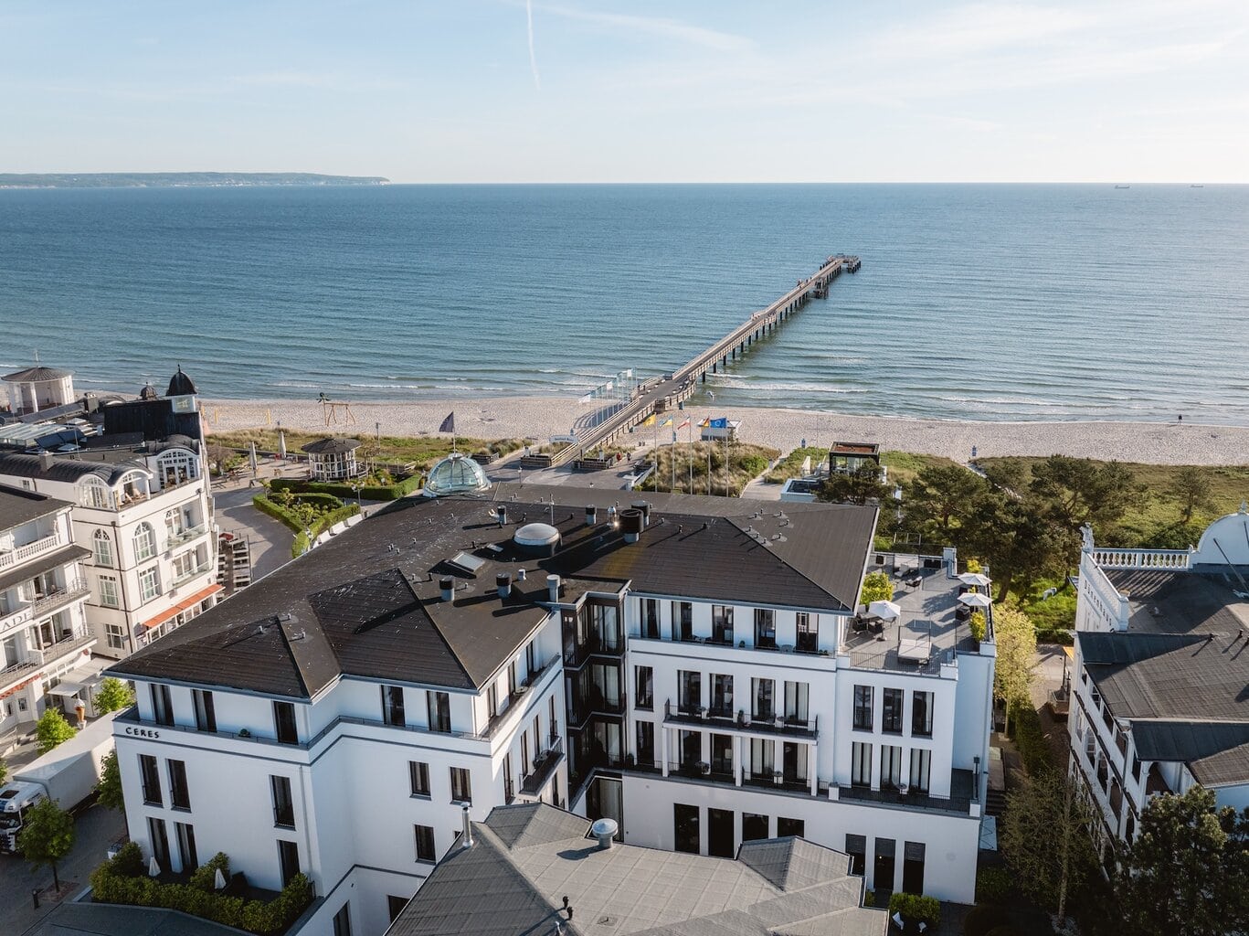 Het Hotel A-ROSA CERES van buiten. Op de achtergrond bevindt zich het Strand van de Oostzee met een steiger.