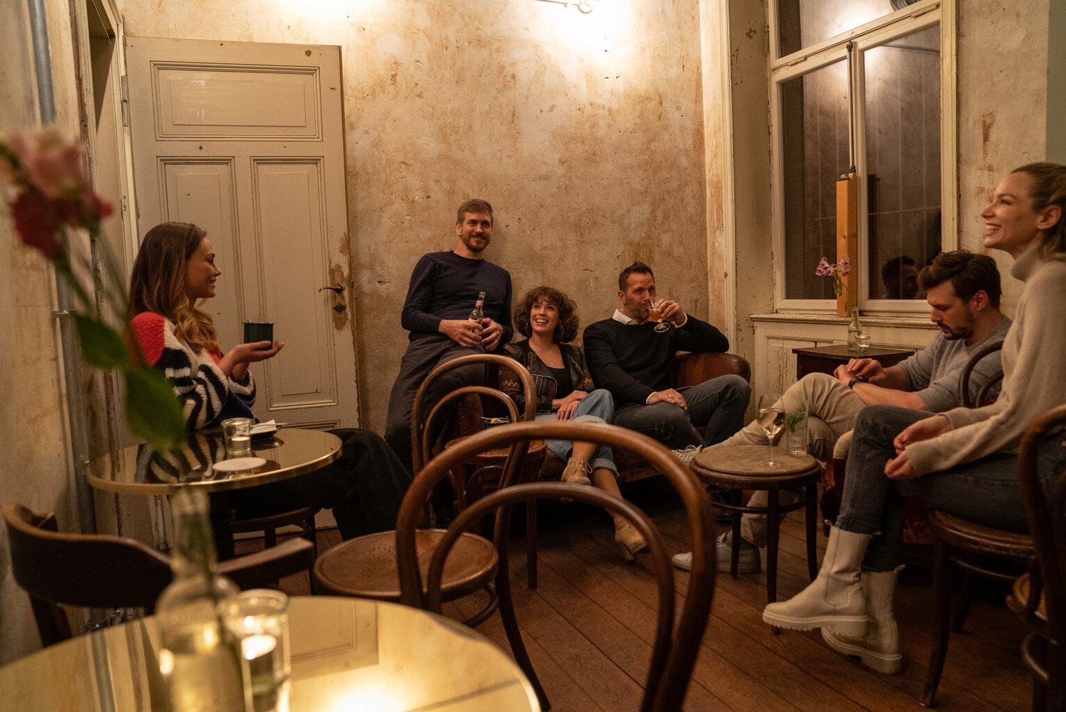Vrienden lachen en drinken in een sfeervol café met vintage muren en zacht licht, een intiem begin van een ontspannen Stuttgart party.