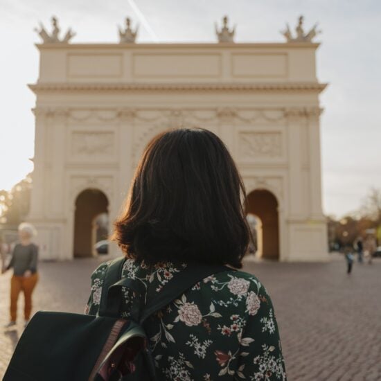 Een vrouw met rugzak kijkt naar de Brandenburger Tor in het zachte avondlicht, waar geschiedenis en rust samen een van de bijzondere Geheimtips Potsdam vormen.