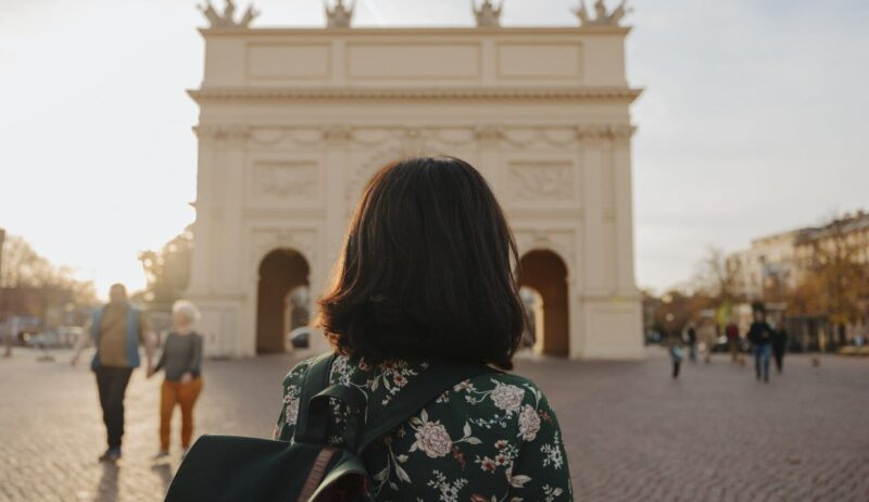 Een vrouw met rugzak kijkt naar de Brandenburger Tor in het zachte avondlicht, waar geschiedenis en rust samen een van de bijzondere Geheimtips Potsdam vormen.