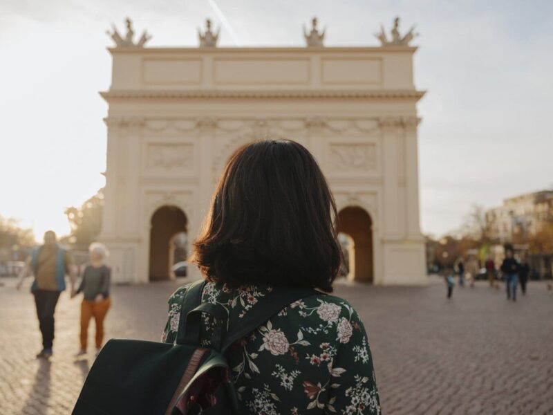 Een vrouw met rugzak kijkt naar de Brandenburger Tor in het zachte avondlicht, waar geschiedenis en rust samen een van de bijzondere Geheimtips Potsdam vormen.